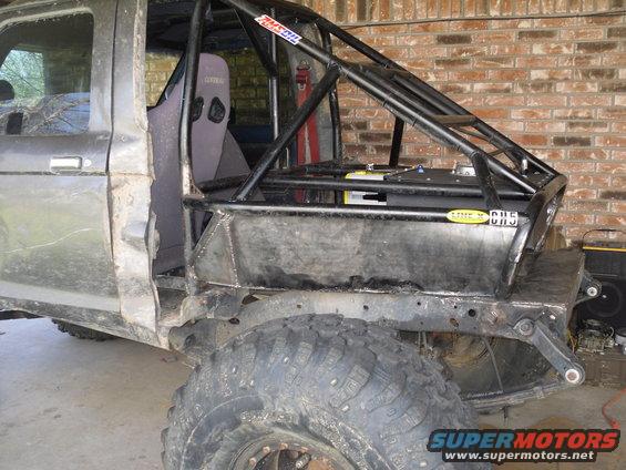 Modified off-road vehicle, dark gray, side view, showing custom roll cage, racing seat, and large tires