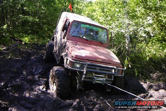 Red Suzuki Samurai stuck in mud, winch cable attached