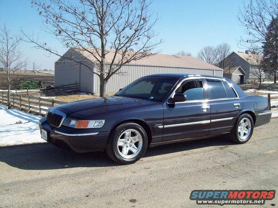 Dark blue sedan parked on a dirt road with a barn and trees in the background