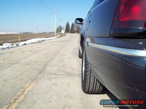 Black 1999 Mercury Grand Marquis rear quarter panel and wheel on a rural road