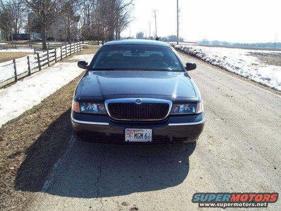 Dark sedan parked on a rural road, front view. Grille and headlights are visible