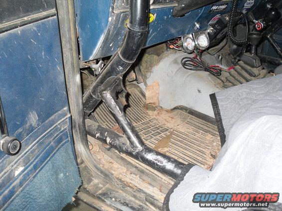 Interior shot of a vehicle showing a roll cage, floor mats, and some gauges