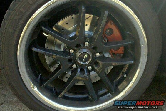 Black five-spoke wheel with orange brake caliper and slotted rotor