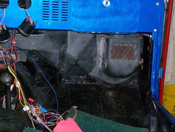 Jeep interior showing dashboard, heater box, and wiring harness. Green carpet and black textured floor are visible