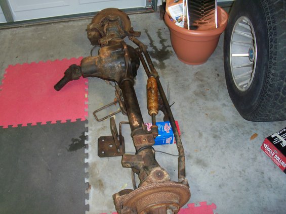 Rusty front axle assembly with shock absorber and steering linkage, on a garage floor