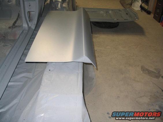 Car door or fender panel, primed and ready for paint. Trunk lid is open in the background