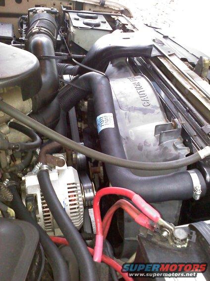 Engine bay with alternator, radiator fan, and battery terminals visible