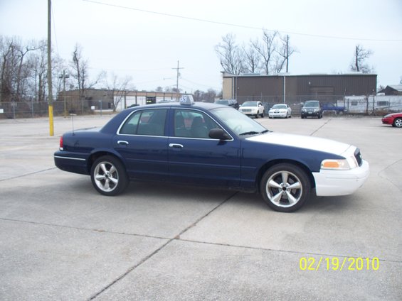 Blue and white 2005 Ford Crown Victoria taxi with a roof light, parked on concrete