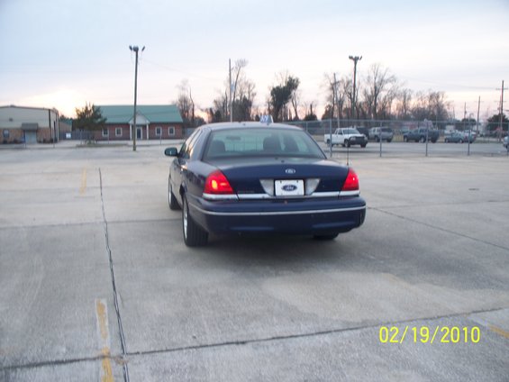Dark blue Ford Crown Victoria parked in a lot. Rear view shows taillights and license plate