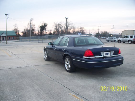 Dark blue sedan parked on concrete, rear view. Chrome trim, aftermarket wheels, taxi light on roof