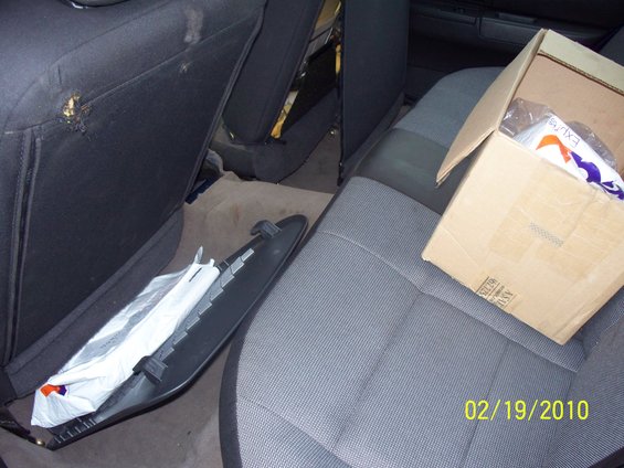 Interior of a car showing the back seat with a cardboard box on it and a detached trim piece on the floor