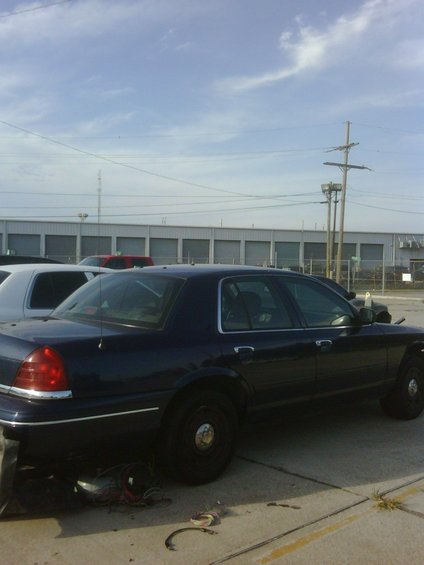 Dark blue 2005 Ford Crown Victoria sedan parked on asphalt, side view, with a white vehicle to its left