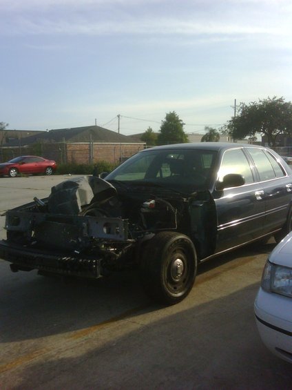 Dark sedan, front end missing parts, parked next to a white car