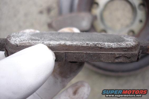 worn brake pad held by gloved hand, rotor visible in background