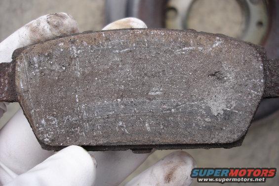 Worn brake pad held by gloved hands, showing scoring and dust