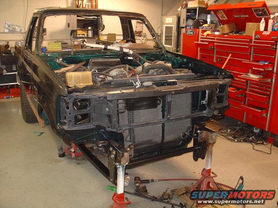 1995 Ford Bronco front end disassembled on jack stands in a garage, engine exposed