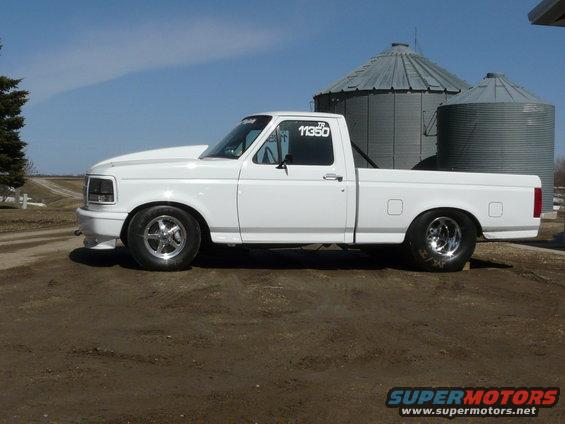 White 1994 Ford F-150 pickup truck with aftermarket hood and racing tires, parked outdoors