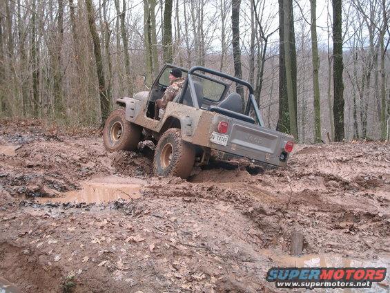 Gray Jeep CJ-7 navigating a muddy trail, rear view