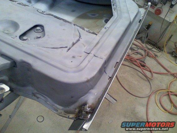 Close-up of a vehicle's lower door frame and rocker panel undergoing repair, showing primer and rust