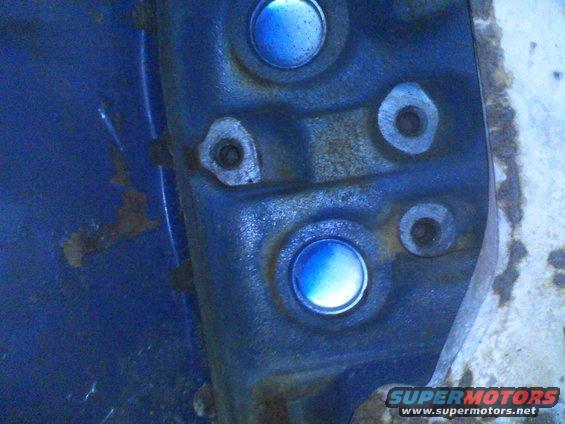 Close-up of blue caps and bolt holes on a blue metal surface with Supermotors logo