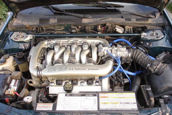 Engine bay of a 1995 Ford Taurus SHO, showing the 24 valve DOHC engine with silver intake runners and blue hoses
