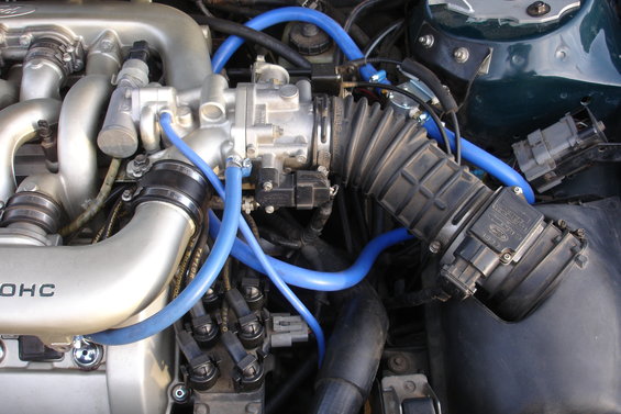 Close-up of engine bay with silver intake manifold, black air intake boot, and bright blue hoses. Some text is visible on the manifold