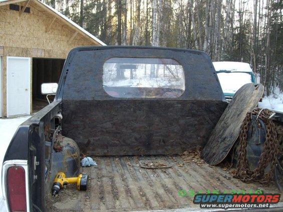 Black truck bed interior with plywood lining, yellow drill, and chains