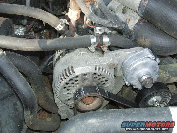 close-up of engine parts, showing an alternator, belt, and hoses