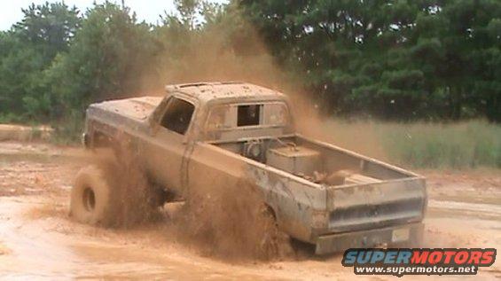 Muddy pickup truck driving through a mud pit, kicking up dirt