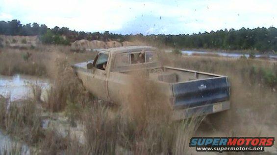 Pickup truck stuck in mud and tall grass. The truck appears to be from the 1980s