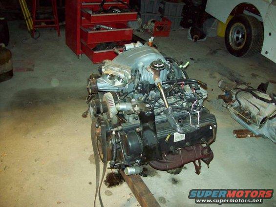 Engine and transmission assembly on a stand in a garage, with a red tool chest in the background