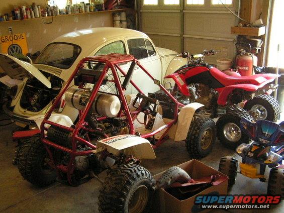 Garage scene with a red go-kart, two ATVs, and a cream-colored VW Beetle