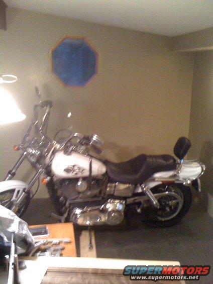 White motorcycle parked indoors, side view. Has a windshield and a passenger backrest