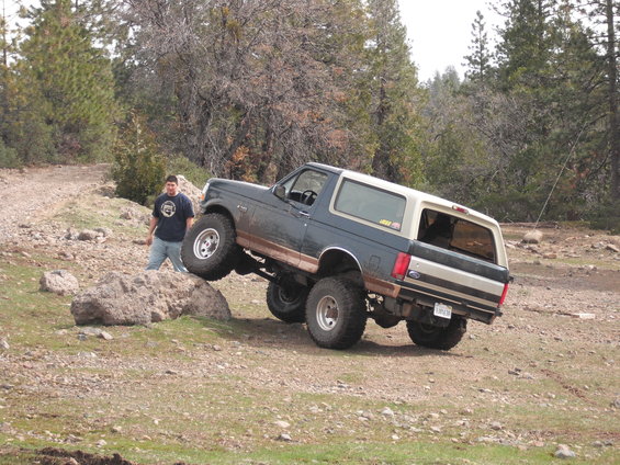 1991 Ford Bronco driving off-road, lifted suspension, dark blue and tan