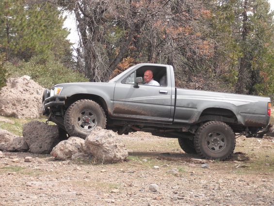 Gray pickup truck with off-road tires navigating large rocks on a dirt path