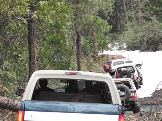 Rear view of a 1991 Ford Bronco driving on a snowy trail with other SUVs