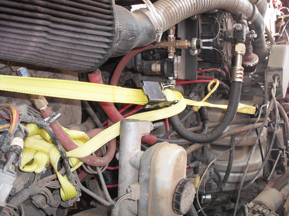 Engine compartment with air filter, hoses, and yellow tie-down strap