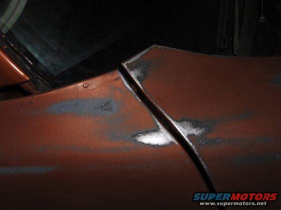 Orange car body panel seam with primer patches and visible metal