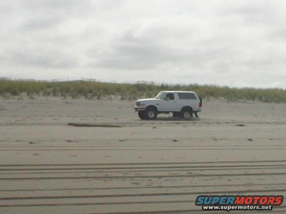 White SUV with spare tire on rear door driving on sand dunes