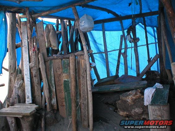 Makeshift shelter constructed from wood and a blue tarp, with various writings on wooden planks