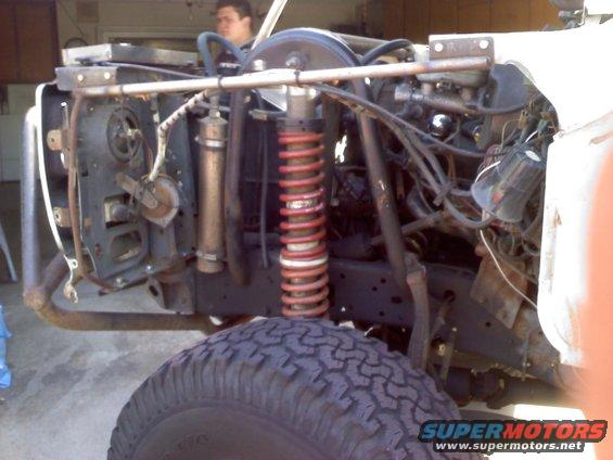 Front tire and disassembled engine bay of a white vehicle with red coil springs