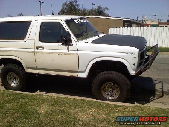 White Ford Bronco with aftermarket bumper and black hood parked on a curb