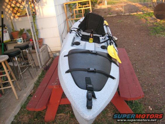 Kayak on a red picnic table, with a beer bottle and yellow paddle. Stools and plants are visible in the background