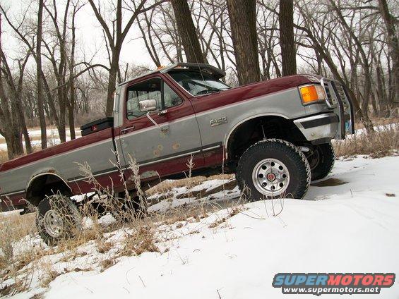 1988 Ford F-150 pickup truck with two-tone paint and a brush guard, parked in a snowy wooded area