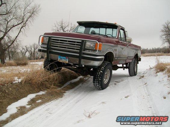 Maroon and silver Ford F-150 pickup truck with a brush guard on a snowy dirt road