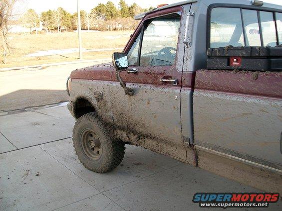 Mud-covered maroon and gray Ford F-150 pickup truck, driver's side 3/4 front view. Visible toolboxes in bed