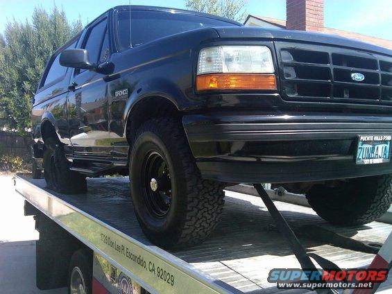 Black Ford Bronco on a tow truck, front right tire visible, license plate reads ZUNBAJA