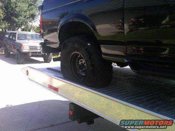 Black SUV's flat tire on tow truck; older SUV in background