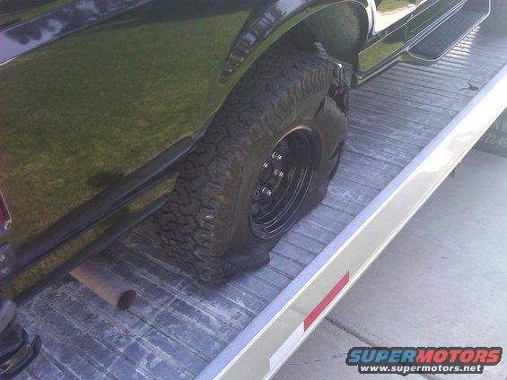Flat tire on a black vehicle being towed on a trailer