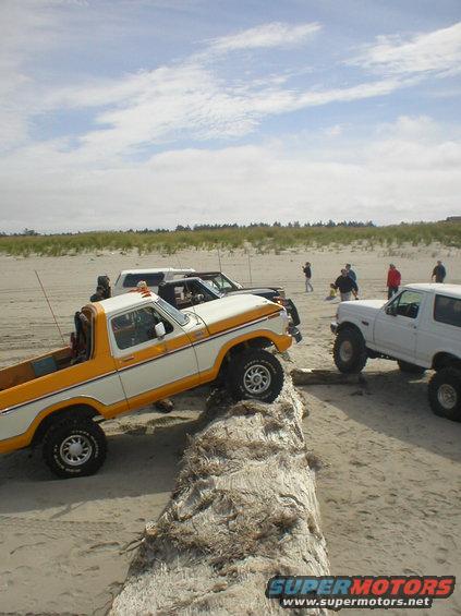 White and orange pickup truck and white Bronco on a sandy beach with people in the background